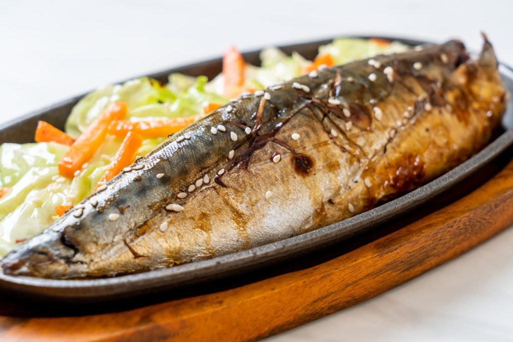 철판 위에 노릇하게 구워진 고등어 구이와 곁들여진 양배추, 당근 볶음 요리.