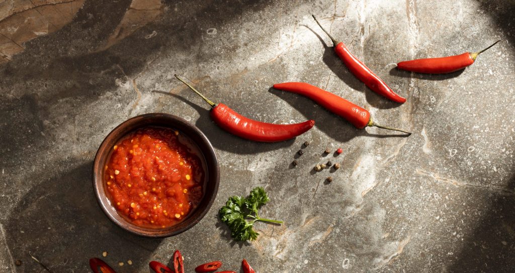 대리석 바닥 위에 놓인 매운 고추 양념장과 신선한 빨간 고추들. 캡사이신이 풍부한 고추는 심부 체온을 높여 야간 가려움증의 원인이 됨