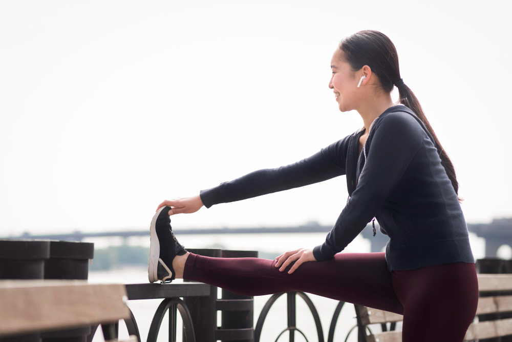 야외에서 다리를 펴고 스트레칭하는 동아시아 여성 — 당뇨 전단계 운동 전 준비 동작, 식후 운동 시작 전 스트레칭