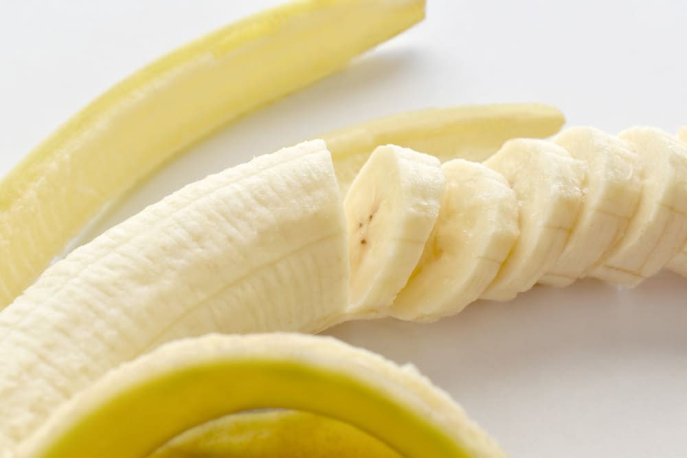 껍질을 벗겨 슬라이스한 바나나 — 한 개(120g)당 칼륨 440~500mg, 고칼륨혈증 관리 중 하루 한 개 이하 섭취 권장
 Sliced banana peeled close-up – 440-500mg potassium per banana, limit to one per day for hyperkalemia dietary management