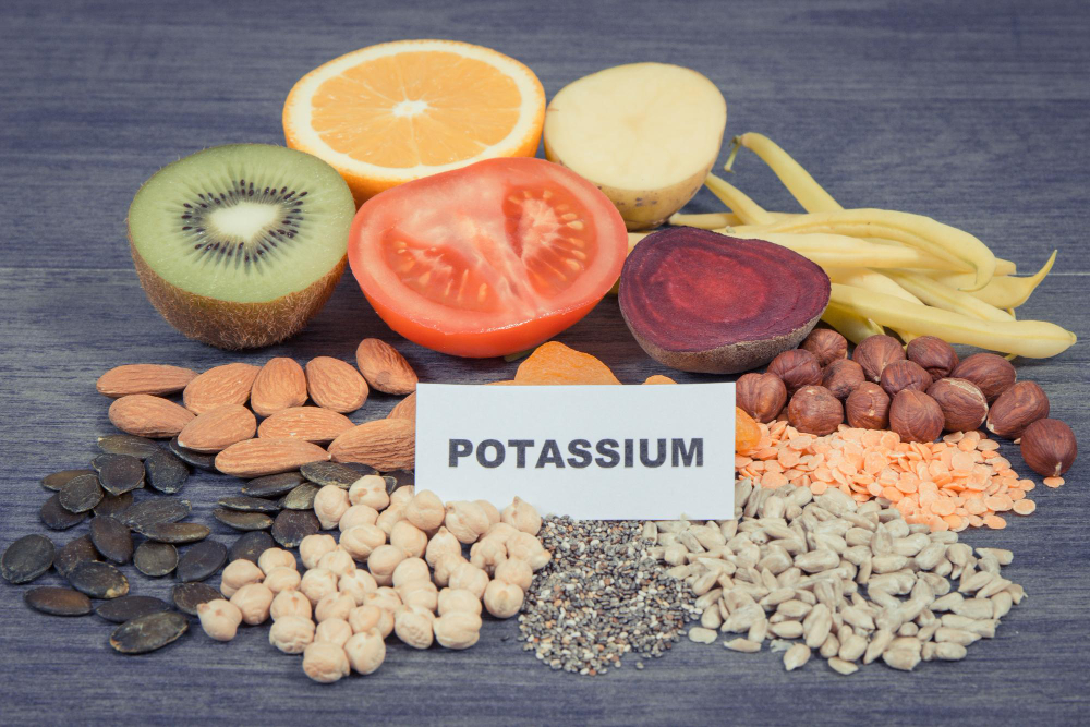POTASSIUM 표지판과 키위·토마토·콩류·견과류 등 칼륨 풍부 식품 — 채식 식단 고칼륨혈증 원인 식품 종류 Potassium label with kiwi tomato legumes nuts and seeds – high potassium plant foods causing hyperkalemia in vegan vegetarian diet