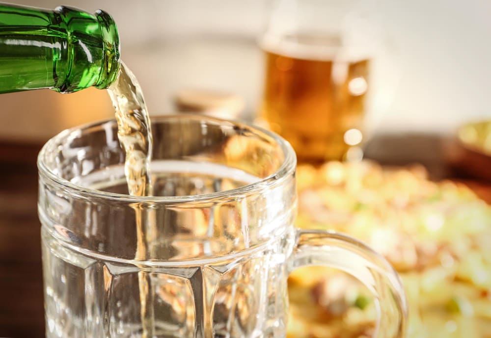 맥주잔에 맥주를 따르는 장면과 배경의 피자 안주 — 음주와 고탄수화물 안주가 혈당 조절에 미치는 영향