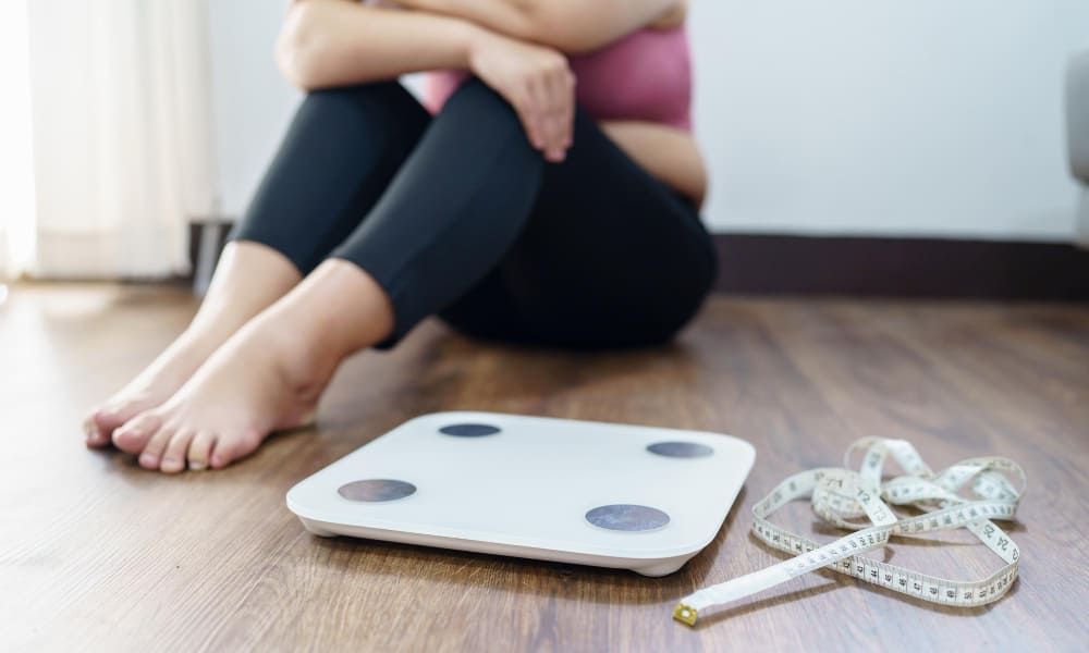 체중계 앞에 앉아 요요를 걱정하는 여성 — 마운자로 치료 후 체중 유지 방법