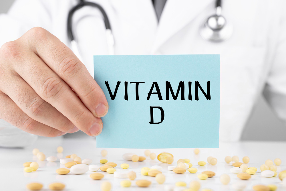 의사가 VITAMIN D라고 적힌 카드를 들고 있고 앞에 각종 영양제가 놓여 있는 모습. 비타민 D는 근섬유 분화와 근수축 기능에 관여하며 결핍 시 근감소를 가속화할 수 있다.