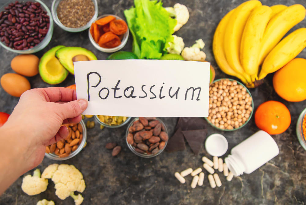 칼륨(Potassium) 표지판과 바나나·콩류·견과류·채소 등 칼륨 풍부 식품 — 채식주의자 고칼륨혈증 신장 기능 저하 주의